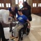 A man with cerebral palsy is seated in a wheelchair in a house of worship. He is preparing to perform ring bearer duties.